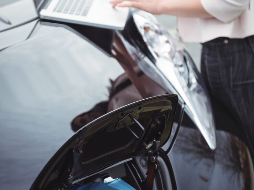 mid-section-woman-using-laptop-while-charging-electric-car_107420-94903